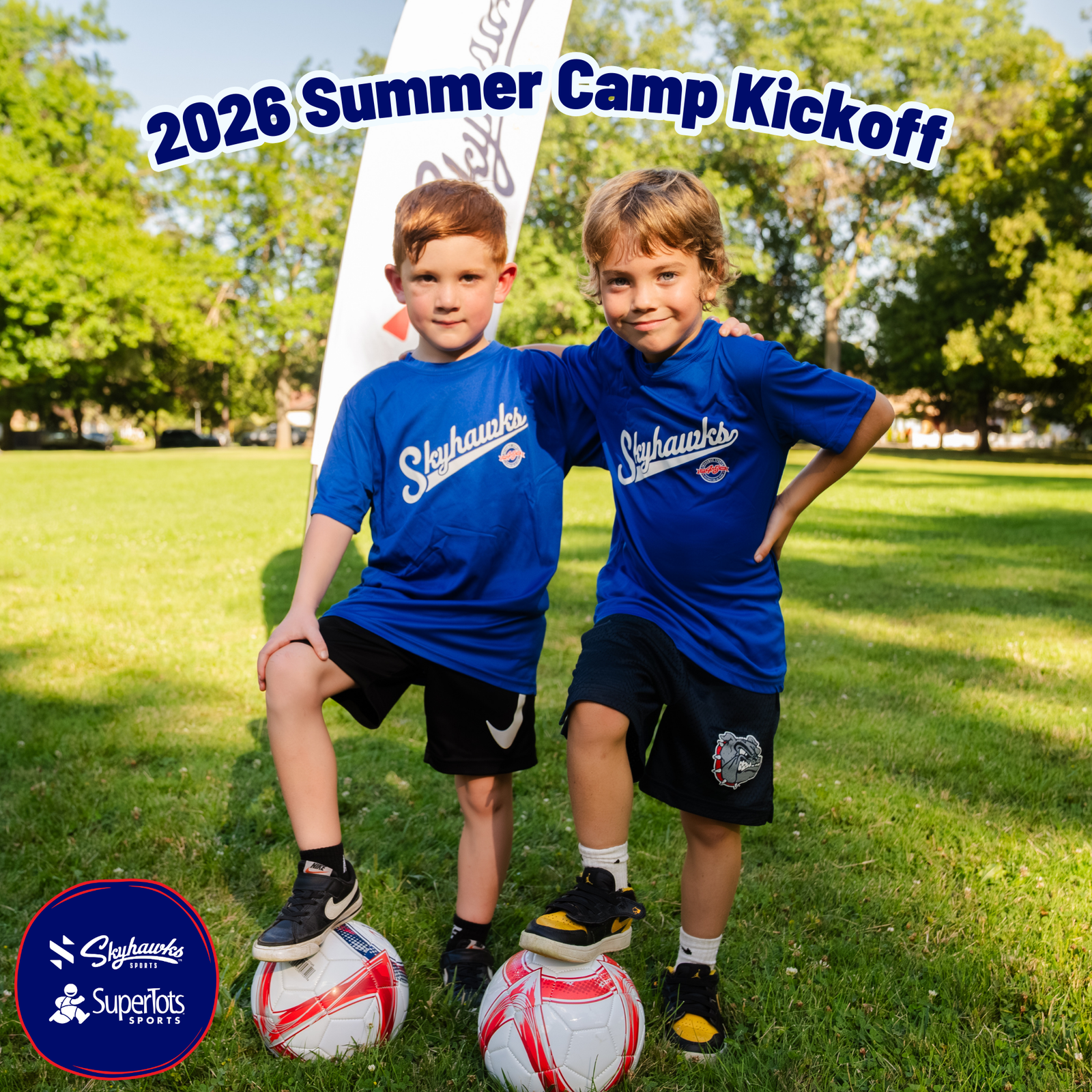Two young boys in blue sports jerseys stand on grass, each with a foot on a soccer ball, smiling at the camera beneath a "2026 Summer Camp Kickoff" banner. - Skyhawks-Supertots Colorado