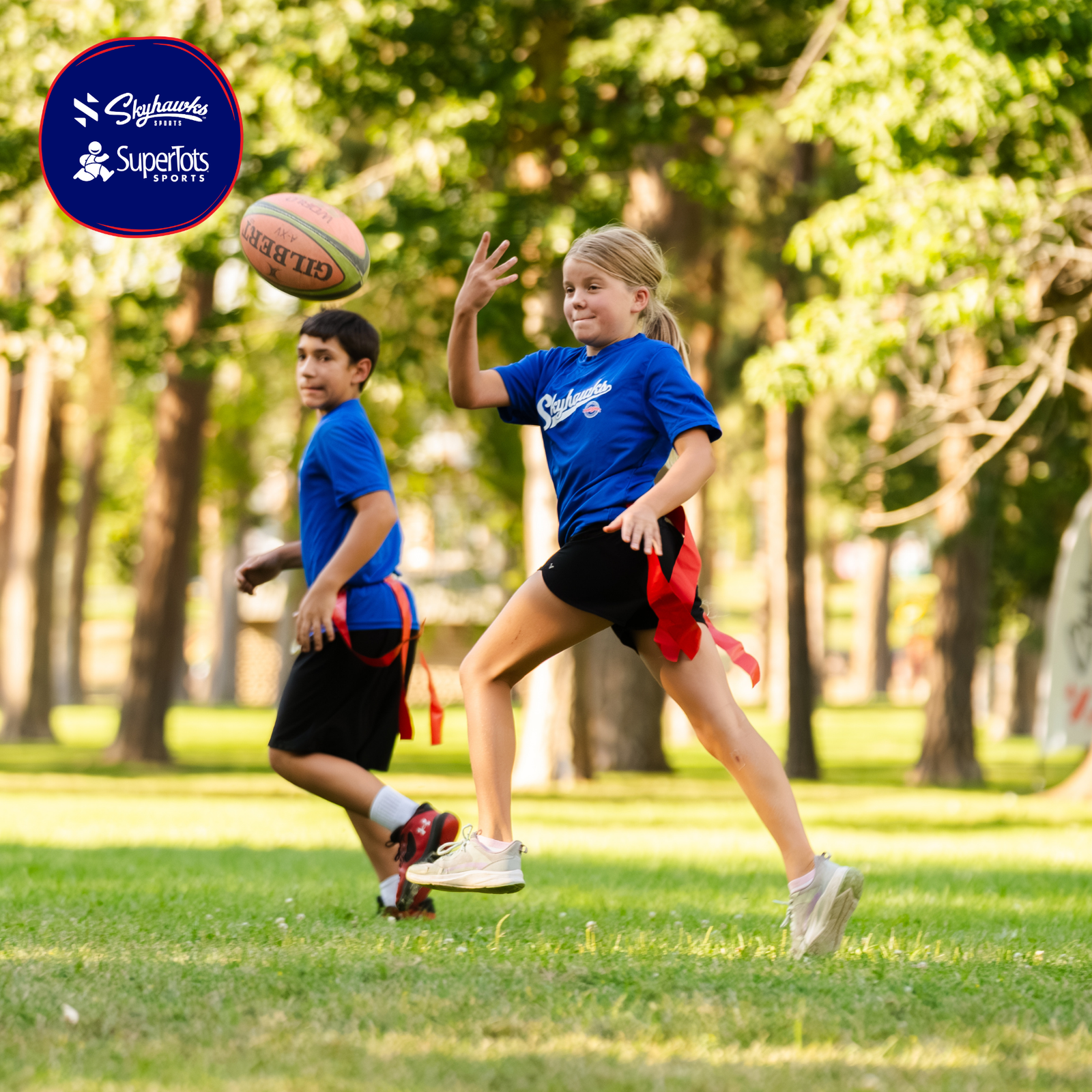 Two children in blue shirts play flag football outside, with one girl preparing to catch a football mid-air. The SuperTots Sports logo appears in the top left corner, highlighting fun with Skyhawks programs for Summer 2026. - Skyhawks-Supertots Colorado